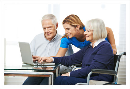 This is a picture of a nurse helping a elderly lady on a laptop, while a older gentlemen is sitting next to her