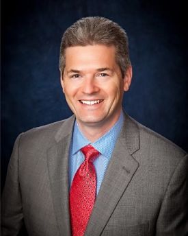 Picture of Troy E. Eller, the new Chief Financial Officer (CFO) at HRMC. He is wearing a gray suit with a blue shirt and red tie.